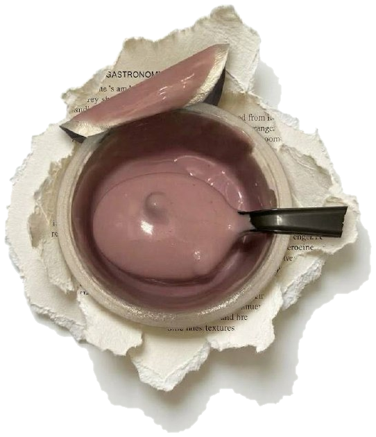 A glass bowl of Forager Project blueberry cashew yogurt resting on a torn printed page, with a spatula lifting a scoop above it