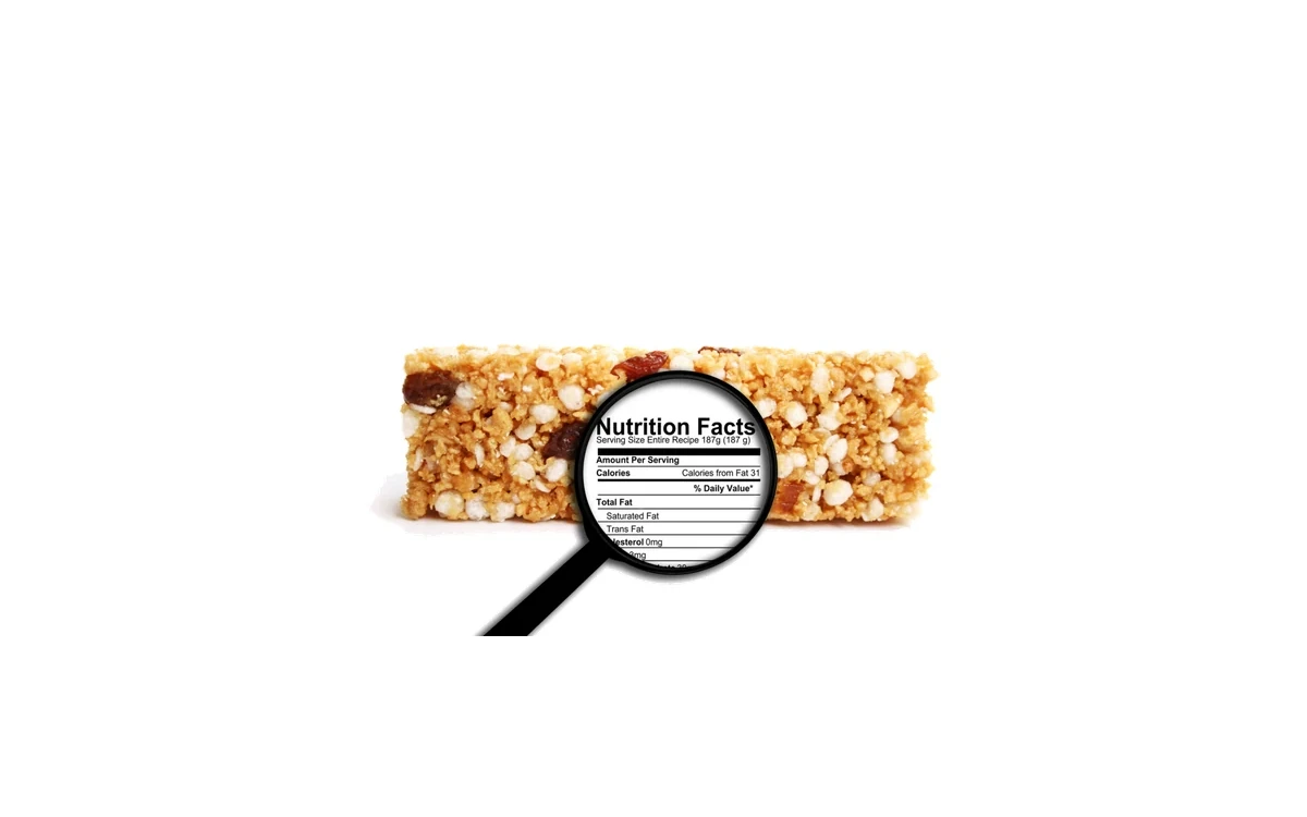 A granola bar with a black magnifying glass resting on it, the lens showing a Nutrition Facts label so you can read what is actually in it.
