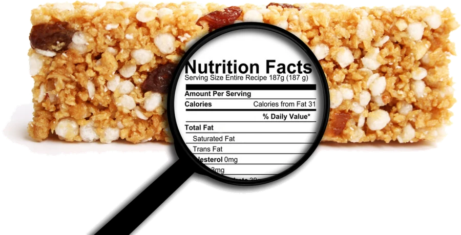 A granola bar with a black magnifying glass resting on it, the lens showing a Nutrition Facts label so you can read what is actually in it.